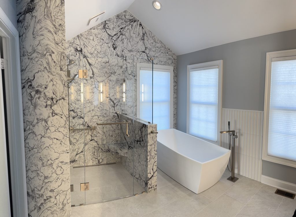 A bathroom with glass shower, deep tub, and grey walls